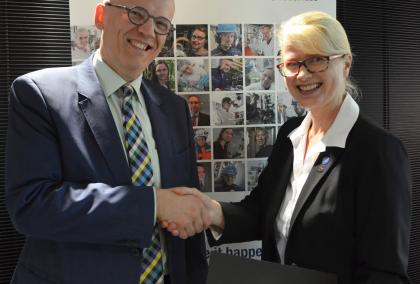VTT CEO Antti Vasara and Fulbright Finland Foundation CEO Terhi Mölsä smiling and shaking hands in front of VTT poster after signing the agreement