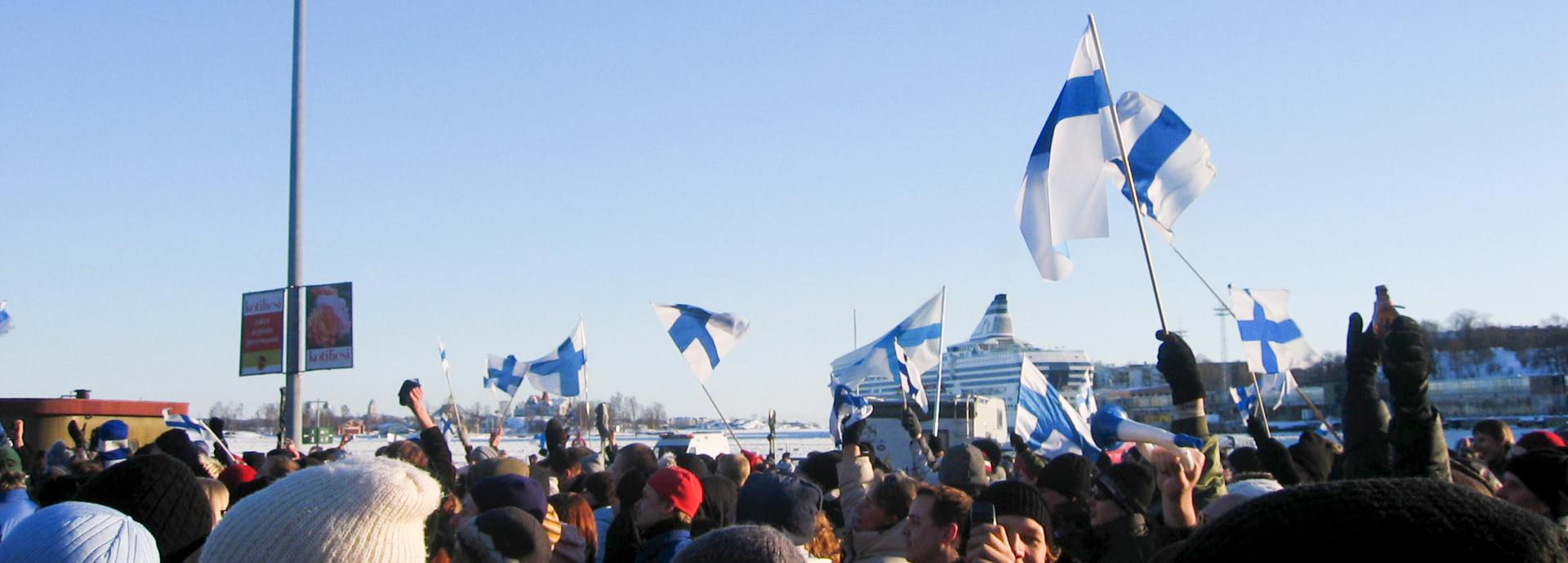 A big crowd of people at the Helsinki Market Square during winter waving Finnish flags