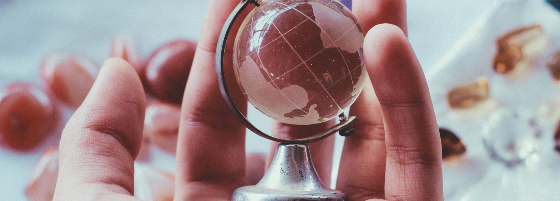 A person holding a globe made of glass in their hand.