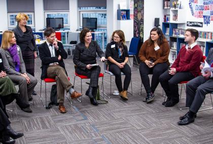 People sitting in a circle. One woman is explaining something with a smile on her face while others are listening to her.