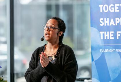 Farida Vis giving a keynote lecture in Maijansali at the Helsinki Central Library Oodi. Behind her is blue Fulbright Finland Foundation roll-up with the words Together Shaping the Future.