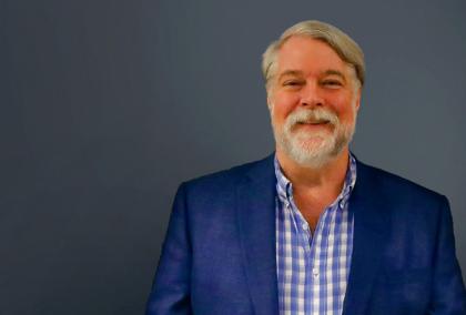 Bill Eaton smiling in front of a grey background