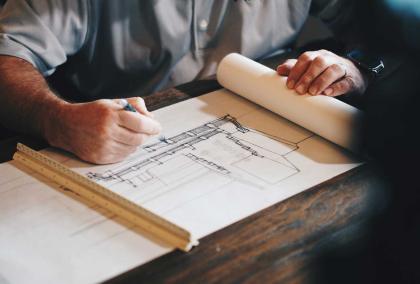 An architect drawing a plan on a paper, there is a ruler on top of the plan.