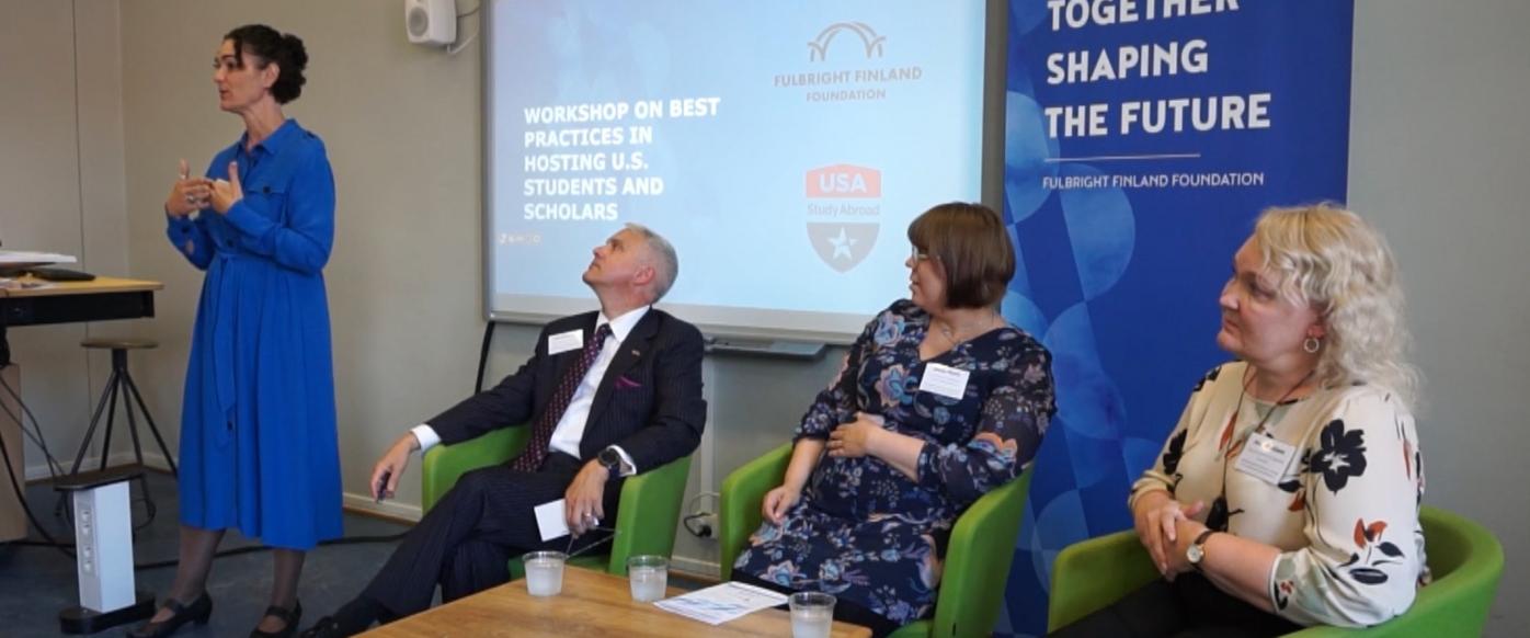 Leasa Weimer moderating a panel discussion about hosting practices. Three panelists, a man and two women, are sitting on green armchairs in front of a classroom.