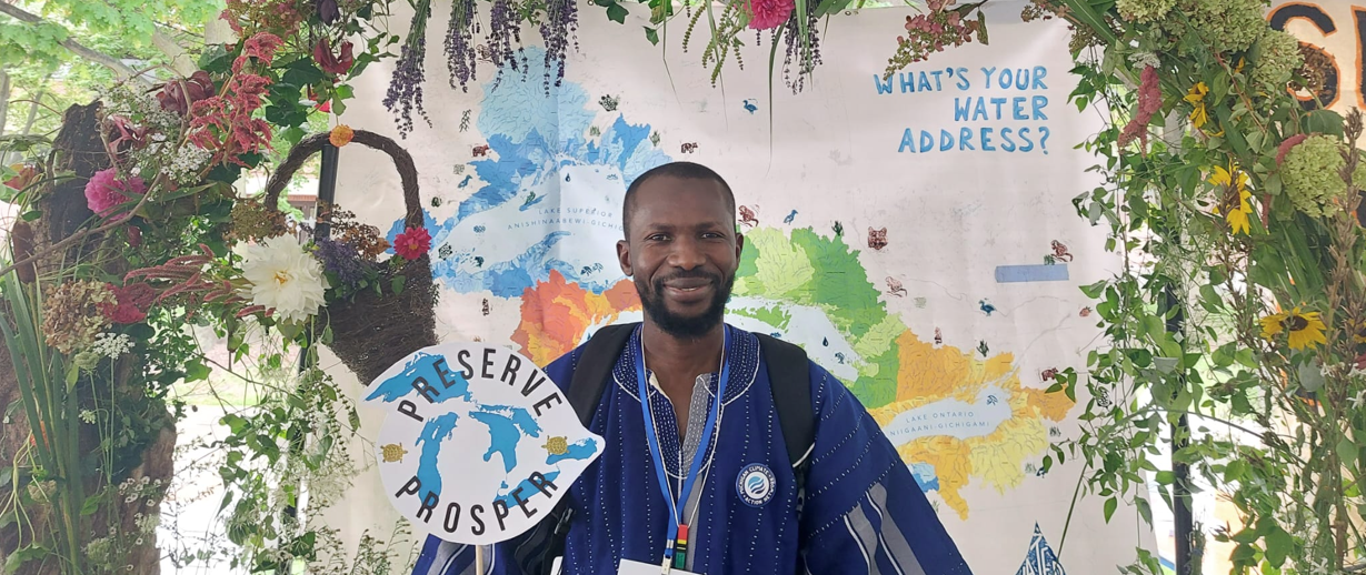 Larry Abdullai holding a sign saying "preserve - prosper", surrounded by a big, flowery arch