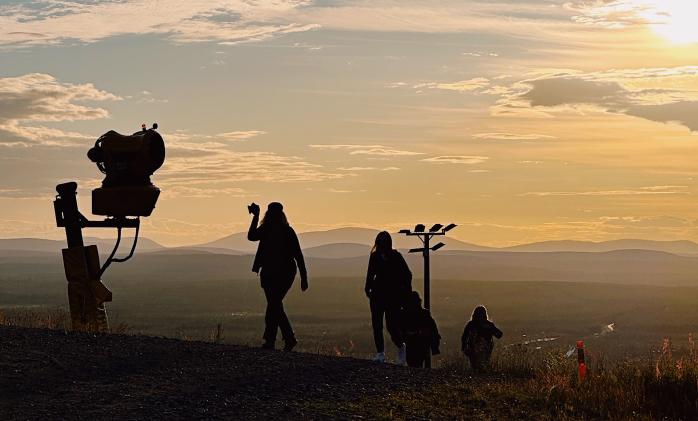 Silhouettes of three people walking up to a fell during a midnight sun.