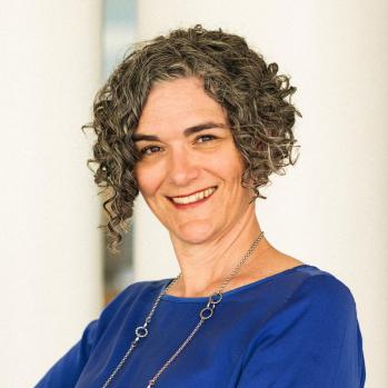 Person with dark, short curly hair and blue shirt smiling