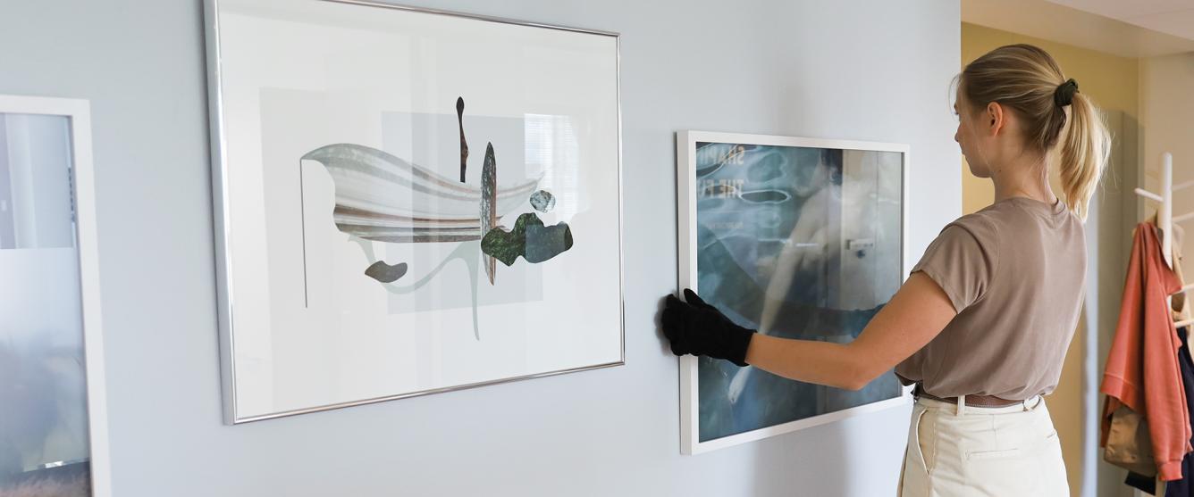 Fulbright Finland alumna Lotta Lemetti hanging a photograph from her award winning project Kekta on the new Fulbright Finland Foundation office wall. The wall already has two of her works on the left.