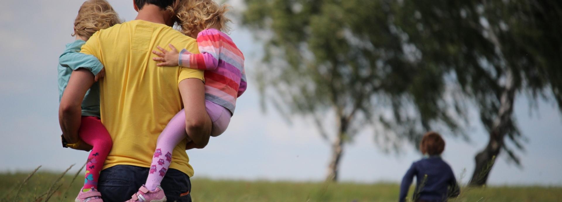 A man carrying two girls on a field of flowers