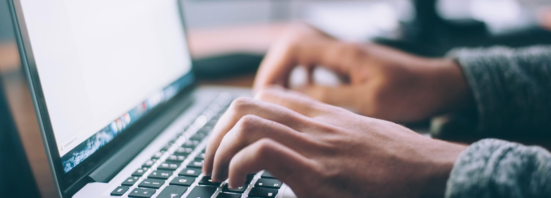 A person using a MacBook laptop. The photo shows hands over the keyboard.