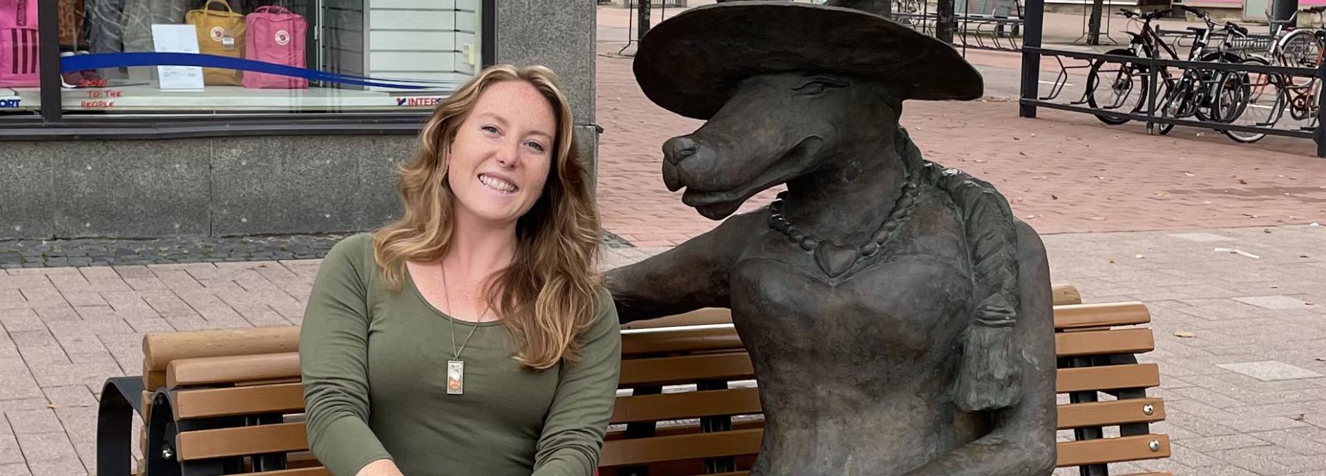 Claire Ramsey next to a wolf statue sitting on a park bench in Joensuu