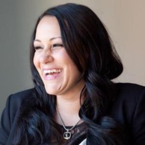 Photo of a laughing woman. She is not looking at the camera but to the left. Wearing a black suit jacket