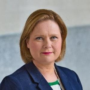 Woman with light brown hair wearing a blue jacket and white-green shirt