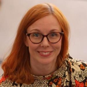 Person with red hair, glasses and yellow-orange flower dress